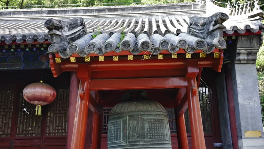 In a Chinese-style courtyard, a large bronze bell hangs in a bright red pavilion.