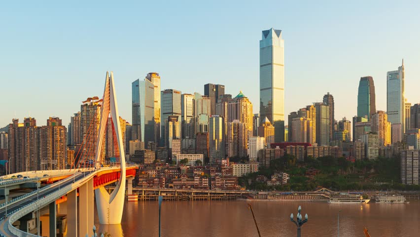 Chongqing, China. Aerial view of a city skyline during sunset with a bridge in the foreground. The cityscape is a mix of modern skyscrapers and older buildings.