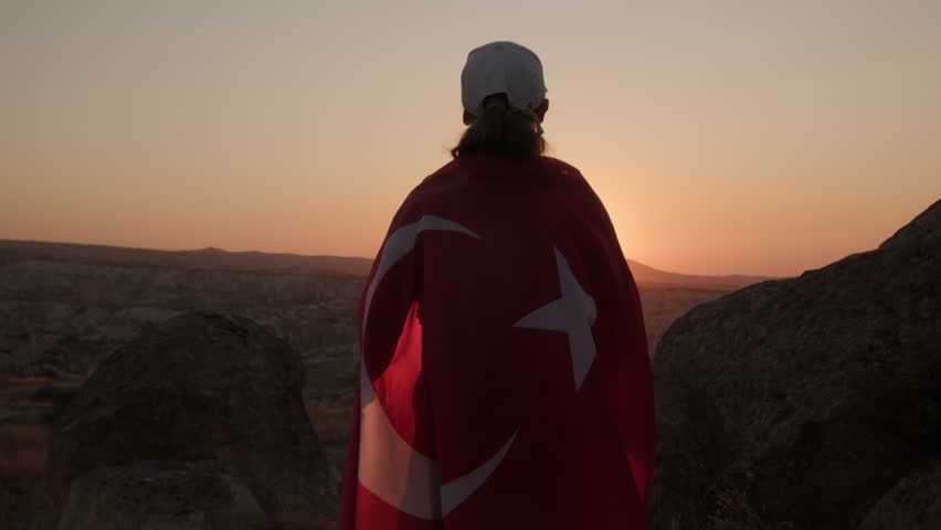 Turkish flag flutters in hands of female tourist at sunset in mountain valley
