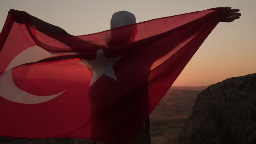 Turkish flag flutters in hands of female tourist at sunset in mountain valley