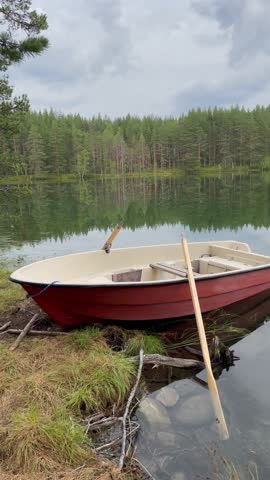 Vertical screen wooden boat with oars near the shore of a forest lake under a cloudy sky calm mood soft light reflection on water cinematic peaceful atmosphere of nature