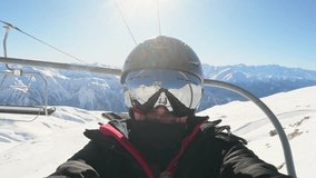 Cheerful young male snowboarder posing for selfie on ski lift surrounded by snow-covered peaks under bright blue sky, enjoying winter holiday and mountain adventure - Powered by Shutterstock - Get 15% off with code: PIKWIZARD15