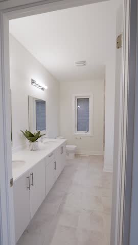 Spacious, bright bathroom with double-sink white vanity, quartz top, twin mirrors and lights, tile floor, window, and toilet—clean, neutral, move-in ready for real-estate listings.