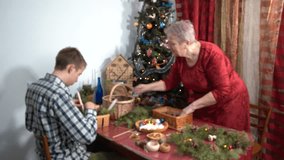 Grandmother and grandson make Christmas decorations together. Elderly woman and teenager boy near Christmas tree. Candles and pine branches Family winter craft - Powered by Shutterstock - Get 15% off with code: PIKWIZARD15