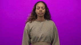 Woman with closed eyes and hands mid gesture in studio wearing cropped sweatshirt against vivid magenta purple backdrop; serenity. - Powered by Shutterstock - Get 15% off with code: PIKWIZARD15