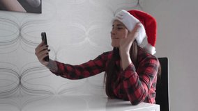 Cheerful young woman wearing a Santa hat makes a video call on her smartphone at home. Cozy holiday atmosphere with warm lighting, festive greetings and joyful emotions.  - Powered by Shutterstock - Get 15% off with code: PIKWIZARD15