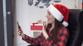 Cheerful young woman wearing a Santa hat makes a video call on her smartphone at home. Cozy holiday atmosphere with warm lighting, festive greetings and joyful emotions.  - Powered by Shutterstock - Get 15% off with code: PIKWIZARD15