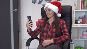 Cheerful young woman wearing a Santa hat makes a video call on her smartphone at home. Cozy holiday atmosphere with warm lighting, festive greetings and joyful emotions.  - Powered by Shutterstock - Get 15% off with code: PIKWIZARD15