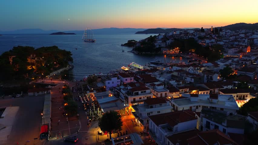 Aerial footage showing the stunning coastline of Skiathos with the sea reflecting warm sunset tones. Boats, harbors, and lush hills frame this idyllic island view