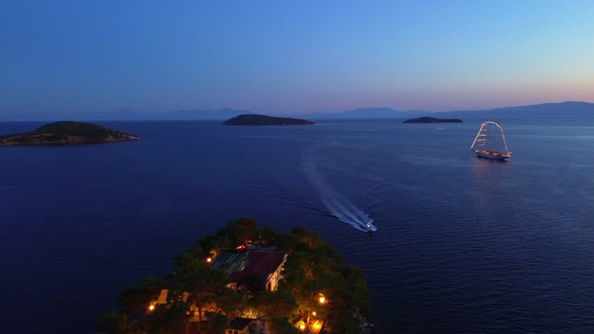 Drone view of Skiathos at sunset, showing the island silhouette and shimmering sea in warm evening light. Peaceful and cinematic atmosphere of the Aegean coast.
