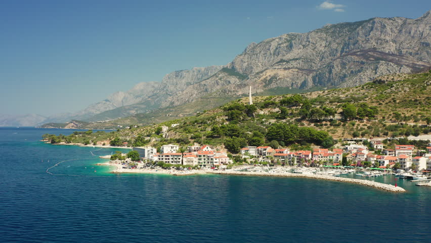 A beautiful travel destination on the Croatian Riviera. This scenic aerial view shows the town of Podgora, its boat harbor, and the majestic mountains meeting the clear Adriatic Sea.