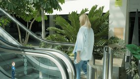 Young businesswoman with blonde hair in casual attire descending an escalator in sunlit business center or shopping mall, attentively using her mobile phone for work or social networking - Powered by Shutterstock - Get 15% off with code: PIKWIZARD15