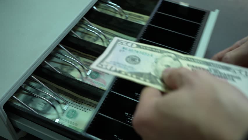 The man opens the cash register with dollars. The cashier puts the dollar money in the cash register and takes the change. Retail for cash DOLLARS