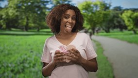 Woman holds a heart shaped gift and sticks tongue while standing on a park path with hands showing a ring; playful joy. - Powered by Shutterstock - Get 15% off with code: PIKWIZARD15