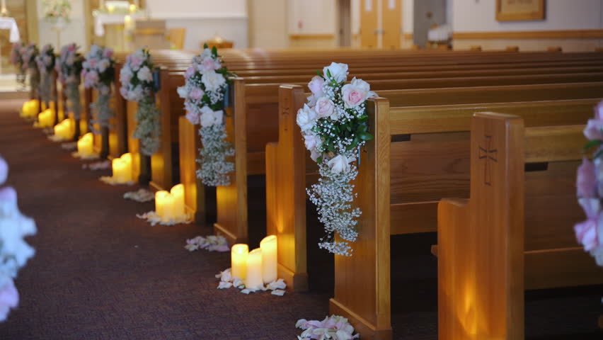 The aisle with flower decorated wooden pews rows in empty church. Christian cathedral interior decoration for the wedding event