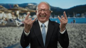 Senior man in suit making rock gesture on beach with ocean in background, blending business with fun in an outdoor coastal setting, expressing joy and confidence. - Powered by Shutterstock - Get 15% off with code: PIKWIZARD15