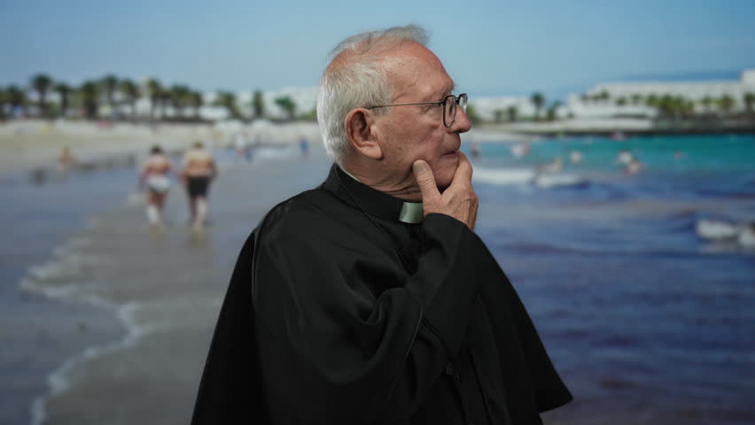 Senior priest in black robe standing by the seaside, contemplating near the water on a sunny beach day, capturing an outdoor, peaceful seaside atmosphere with thoughtful expression.
