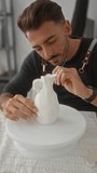 Man leans forward and holds brush to white vase in studio while steadying sculpted ceramic form; serenity. - Powered by Shutterstock - Get 15% off with code: PIKWIZARD15