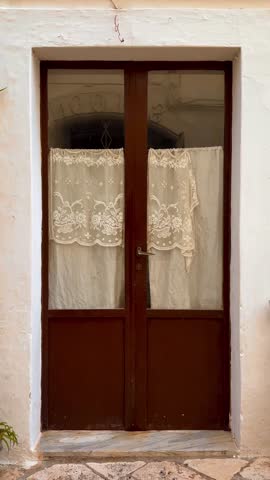 sorry of brown wooden French doors with lace curtains on the inside in Puglia, Italy. November 1, 2024