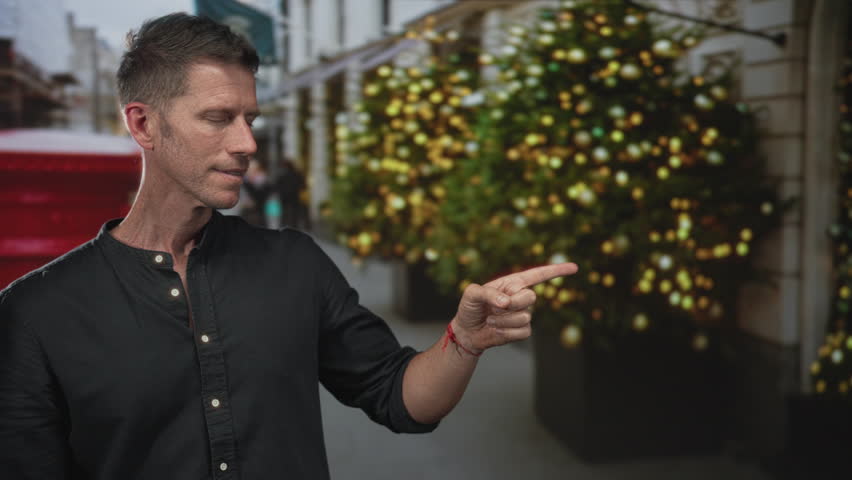 Man points finger on street beside decorated holiday tree, festive lights, and red postbox; curiosity invitation.