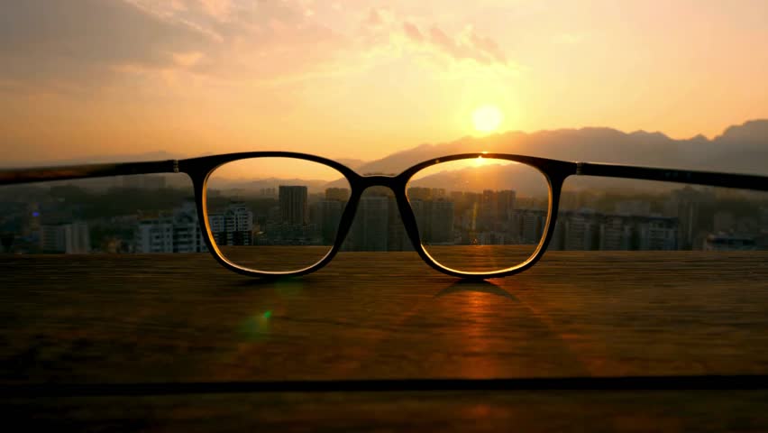 Eyeglasses resting on a table illuminated by the warm glow of a sunset, creating a peaceful and reflective atmosphere.