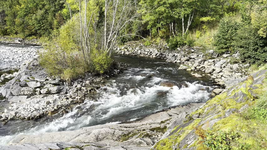 The river flows over rocks and runs near the autum in Norway