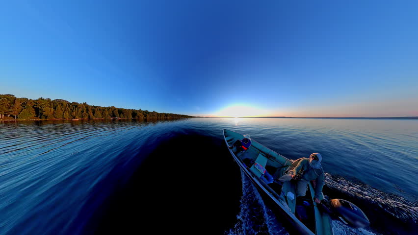 Boat with anglers tourists gliding during golden hour sunset with land skyline silhouetted. Best time for fishing game. View of sun set horizon at lake from boat. Cinematic view of evening leisure.