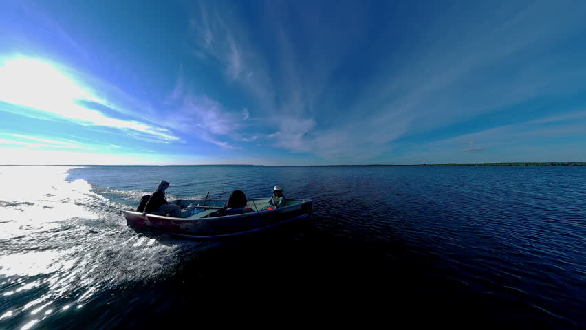 Boat with anglers tourists gliding during golden hour sunset with land skyline silhouetted. Best time for fishing game. View of sun set horizon at lake from boat. Cinematic view of evening leisure.