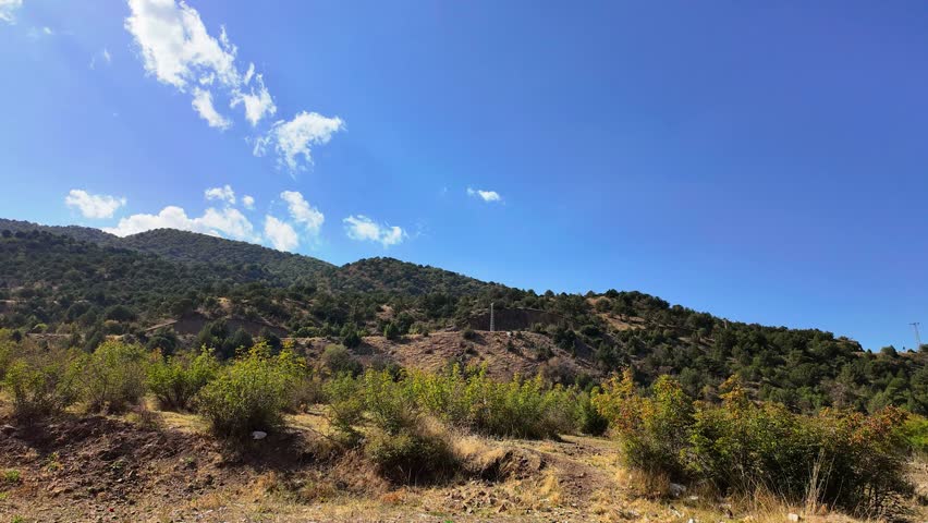 White Clouds Moving Across a Blue Sky Over Green Mountains, 4K Timelapse.