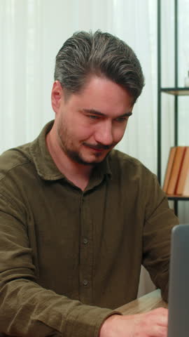 Middle-aged man at home reviews laptop report claps hands pleased winning big deal profit achieved. Young adult guy at table celebrates contract success smiles excited sensing big career boost ahead