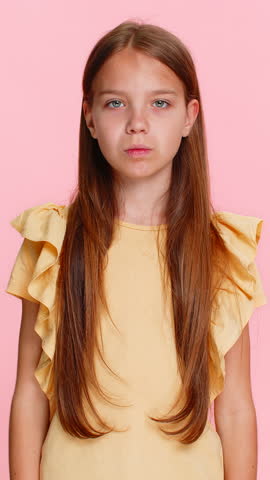Young child girl shakes head disapprovingly clearly shows a strong no gesture with hand, refusing to do something. School kid isolated on pink background emotionally expressing disagreement rejection.