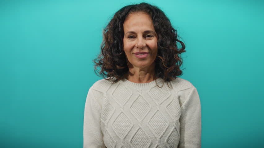 Woman smiling against bright blue backdrop showcasing mature beauty and curly hair in isolated studio setting, perfect for representing hispanic adult female confidence and elegance.