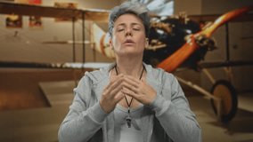 Woman clutch chest by a vintage airplane exhibit in museum building hallway alcove; reflection serenity. - Powered by Shutterstock - Get 15% off with code: PIKWIZARD15