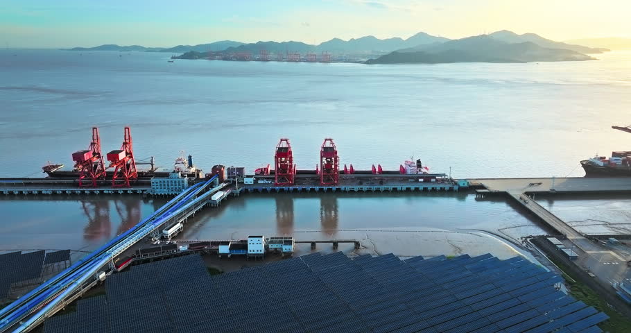 Aerial shot of cargo terminal at a commercial port with large red cranes and a docked ship. Global logistics and transportation background.
