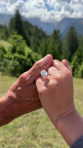 Vertical romantic couple scene in Montenegro highlighting an oval diamond engagement ring and the natural beauty of mountains and greenery surrounding them.