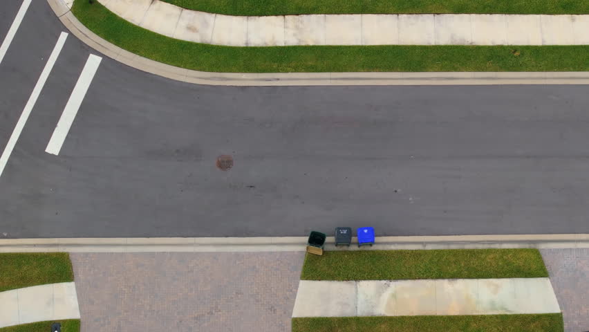 Garbage truck picking up trash bins on suburban street side.