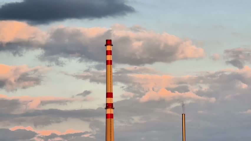 A stunning view of tall industrial chimneys elegantly silhouetted against a vibrant sunset sky filled with clouds