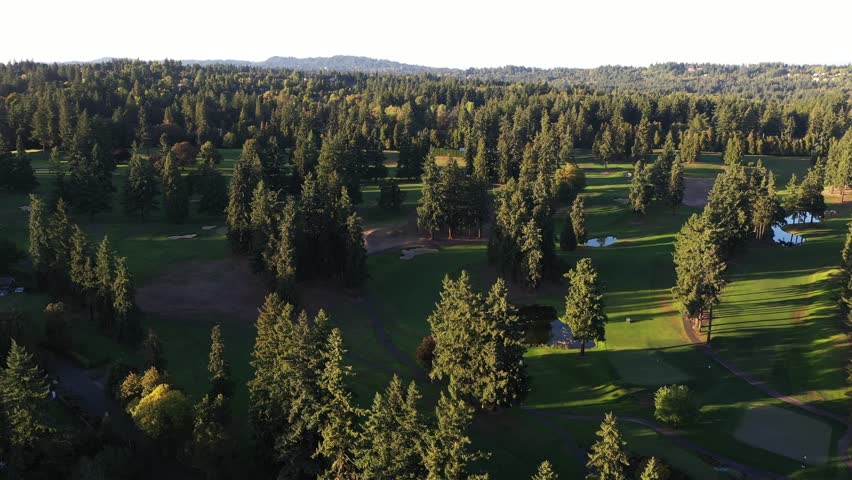 4K aerial drone footage of a golf course surrounded by green forest near Lake Oswego, Oregon. Scenic view of fairways, trees, and open landscape captured from above on a sunny evening in early fall