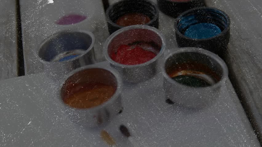 Camera view shifting downward revealing paint cups next to colored brushes showcasing art workspace. Art supplies, creative workspace, colorful palette, studio equipment, abstract design, artistic