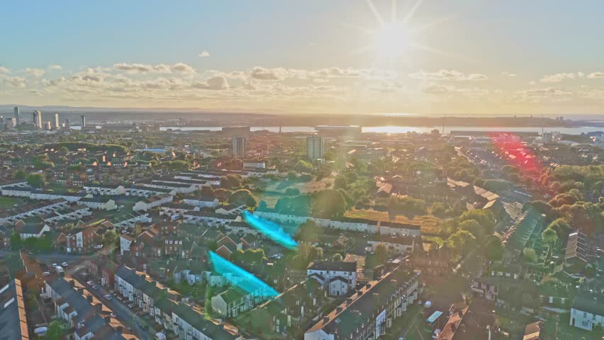 Cinematic aerial drone footage of the neighbourhood surrounding Liverpool FC’s iconic Anfield stadium, captured during sunset. The golden-hour light highlights residential streets, rows of houses.