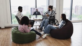 Diverse group of colleagues including man in wheelchair and a woman engaging in virtual meeting with African male speaker on screen, demonstrating teamwork, inclusivity, online collaboration. - Powered by Shutterstock - Get 15% off with code: PIKWIZARD15