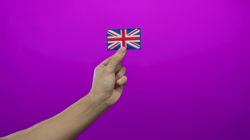 Male hand holds embroidered union jack against pink background, symbolizing great britain identity and cultural pride, isolated with vivid emphasis.