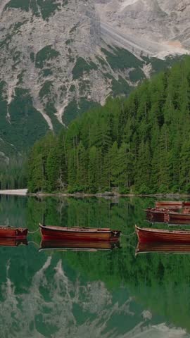 Vertical screen of docked boats and pine forest reflection on Lago di Braies, Dolomites