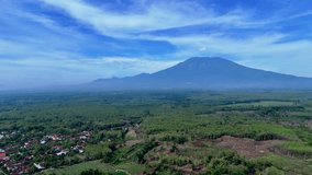 Sweeping drone footage showcasing the massive volcanic mountain dominating the horizon above an extensive tropical teak forest and a foreground of patchwork agricultural fields and rice terraces. - Powered by Shutterstock - Get 15% off with code: PIKWIZARD15