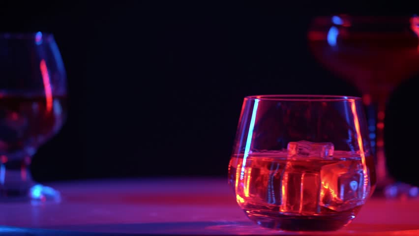 Three glasses with different alcoholic drinks stand on a rotating round table in the neon light of a nightclub or bar.