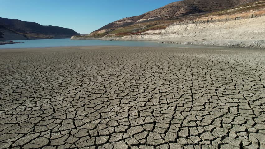 Drone aerial footage of barren land, deep cracks, and  low water in the reservoir. Desolate landscape under a clear blue sky. Impact of drought Cyprus. Climate change

