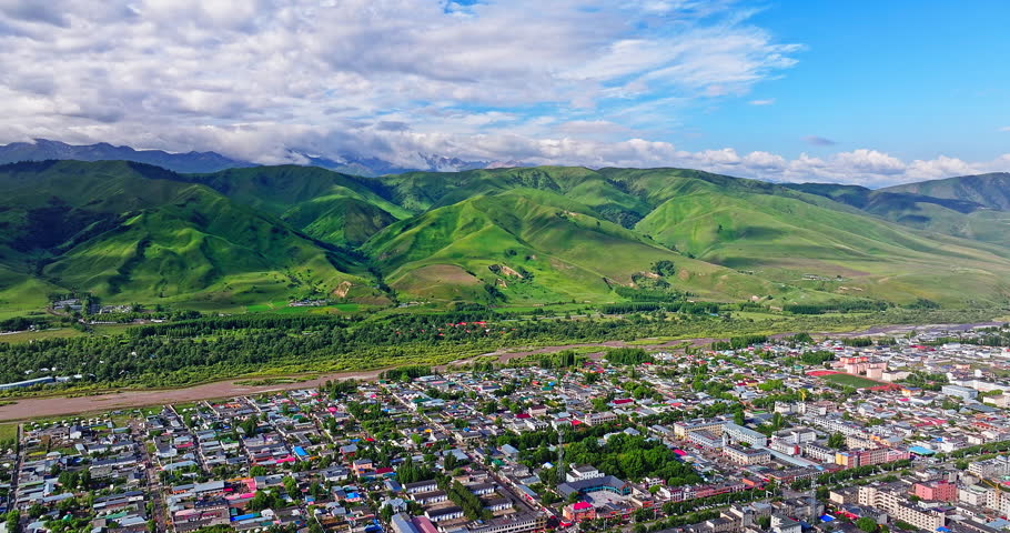 Aerial shot of a scenic town with residential buildings and lush green mountain range in Xinjiang, China.