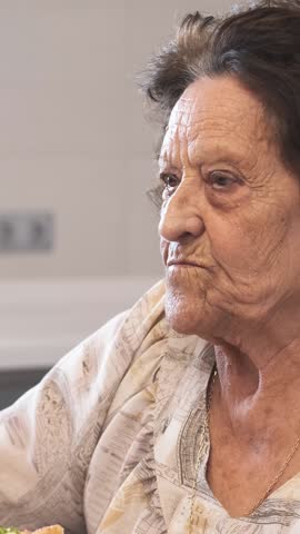 Wrinkled senior woman with short brunette hair looking away while eating delicious open faced avocado sandwich in kitchen