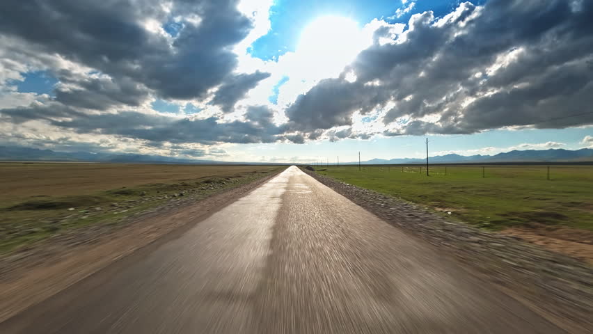 Driving car on a straight country road through vast grassland landscape under cloudy sky