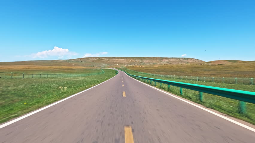 Driving car on a winding asphalt road through vast grassland landscape under blue sky 